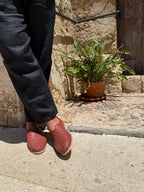 Person wearing lounger cherry huaraches standing on a stone pavement next to a stone wall with a plant.